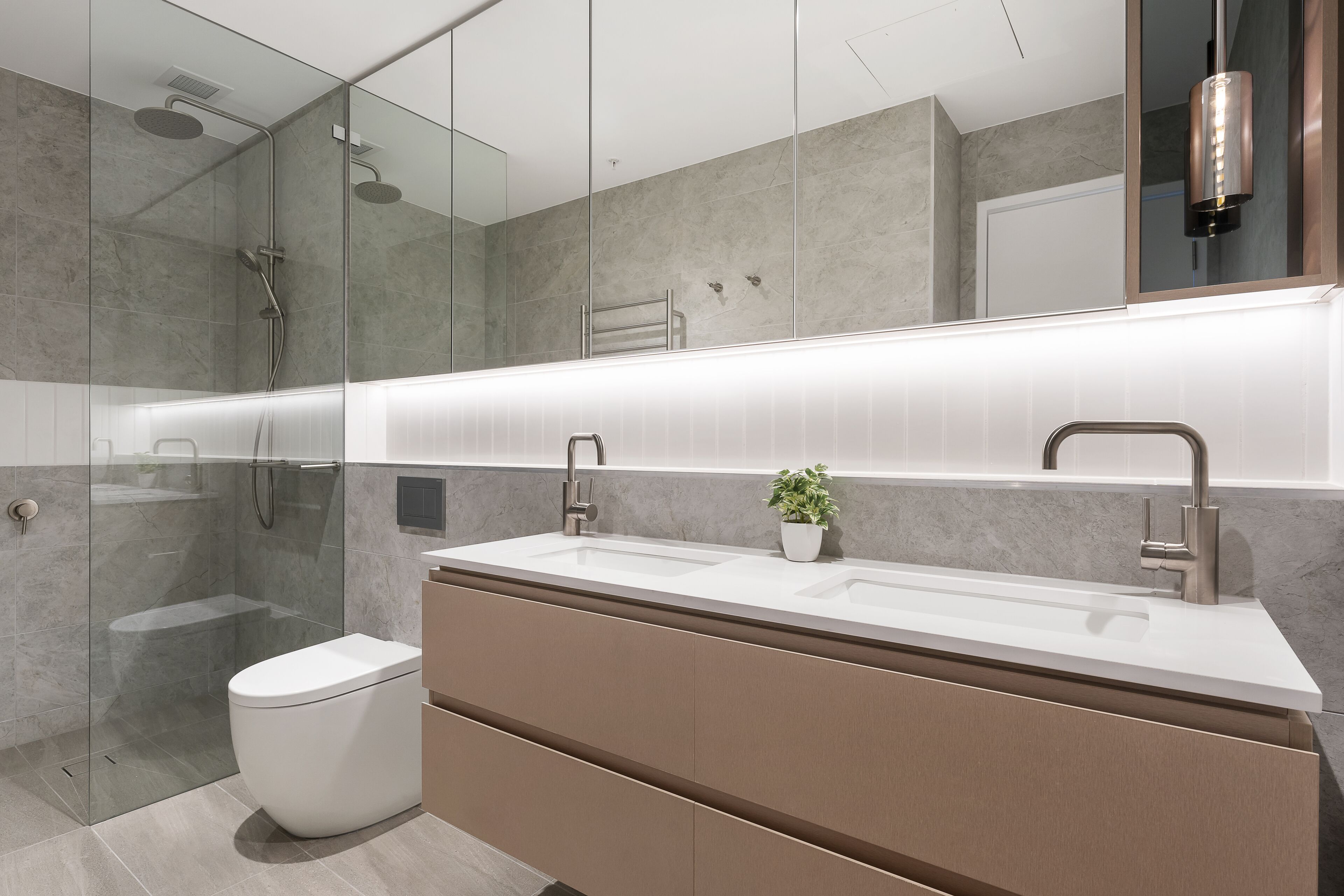 A modern bathroom with a glass-enclosed shower, a white toilet, and a vanity with a sink and mirror.