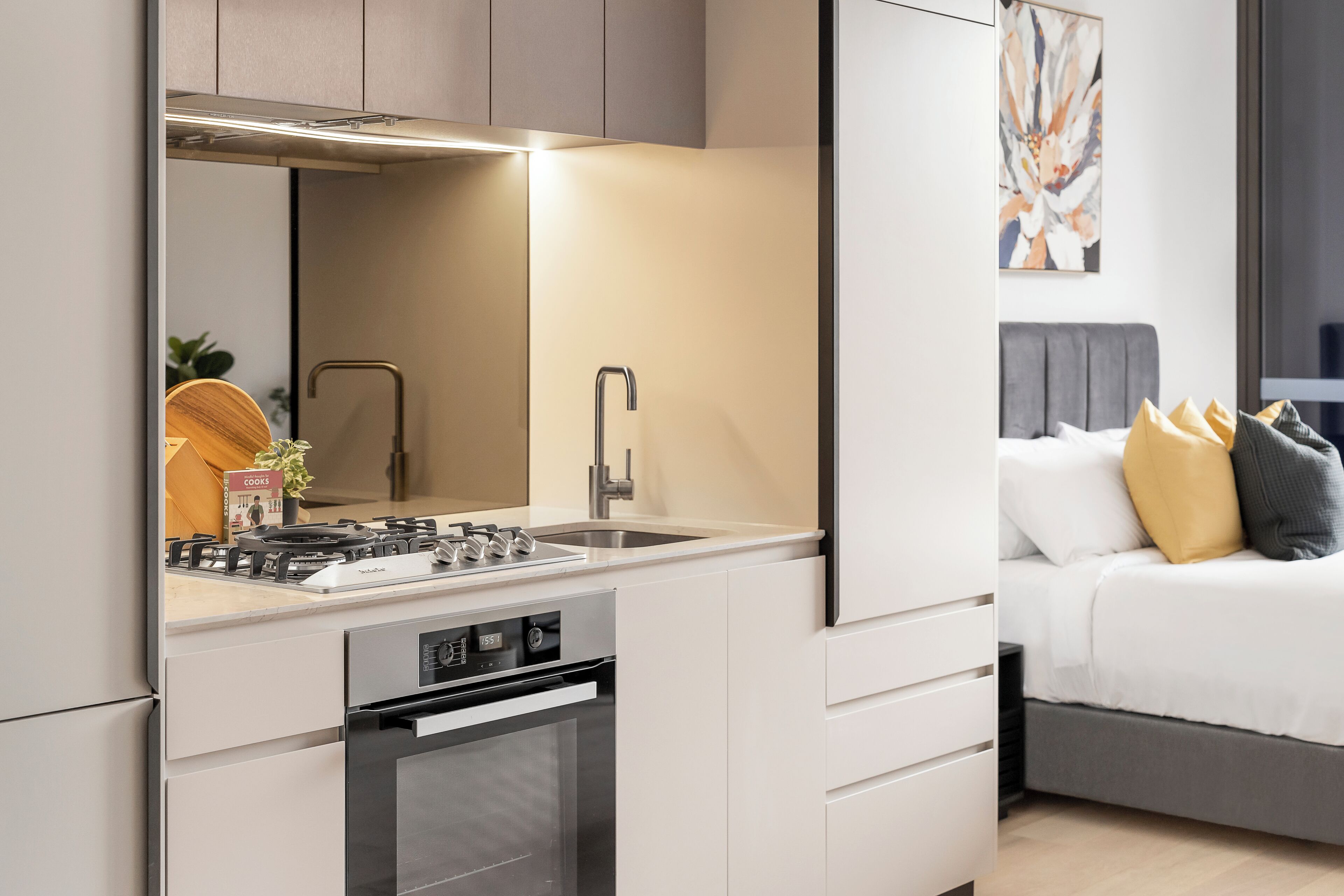 Een moderne keuken met een ingebouwde kookplaat, oven en spoelbak, en een slaapkamer met een bed en kussens.