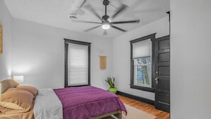A bedroom with a bed, a ceiling fan, two windows, a door, and a small plant. - Gorgeous New Remodel - Close To It Everything! (Indianapolis)