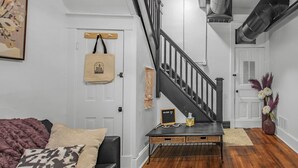 A staircase leading to an upper floor, a wooden bench with a welcome sign, a door with a hanging bag, and a wall-mounted artwork. - Gorgeous New Remodel - Close To It Everything! (Indianapolis)