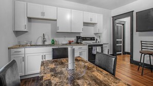 A modern kitchen with white cabinets, a granite countertop, and a dining area with a wooden table and chairs. - Gorgeous New Remodel - Close To It Everything! (Indianapolis)