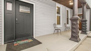A house with a dark front door, white siding, and a porch with two chairs and stone columns. - Gorgeous New Remodel - Close To It Everything! (Indianapolis)