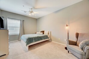 A bedroom with a bed, a chair, a desk, a ceiling fan, and a floor lamp.