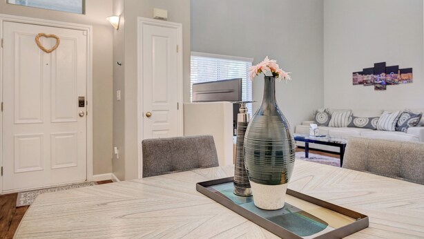 A dining area with a table, chairs, a vase with flowers, and a wall-mounted TV. - Gated Dual Master Suites with Office and Dog Park (Las Vegas)