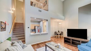 A modern living room with a sofa, a coffee table, a TV, and a staircase leading to a second floor. - Gated Dual Master Suites with Office and Dog Park (Las Vegas)
