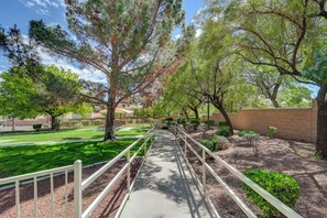 A pathway with a railing, surrounded by trees and a brick wall.