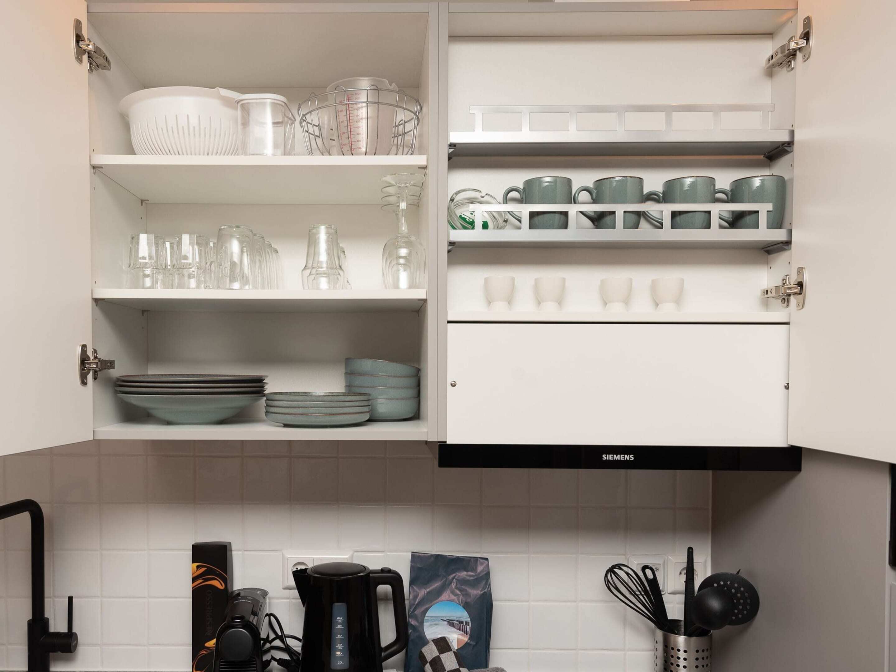 A kitchen with white cabinets, shelves with glassware, plates, and a coffee maker.