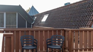 A wooden deck with two chairs and a table, a tiled roof, and a building with a pointed roof in the background. - Studio in Domburg Near Beach and Nature Reserve (Renesse)