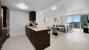 A modern kitchen with a central island, a dining area with a glass table, and a view of the city through large windows. - ICON W BRICKELL SPLENDID OCEAN VIEW 2BR/1BA #1709 (Miami)