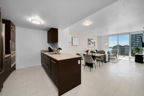 A modern kitchen with a central island, a dining area with a glass table, and a view of the city through large windows.