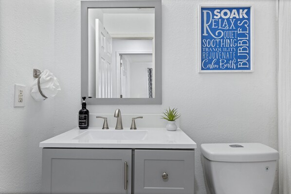A modern bathroom with a white sink, a mirror, and a toilet. There is a sign on the wall with words like "SOAK," "RELAX," and "BUBBLES." - Heated Pool Option, Close to Freeway, Hiking & Golf nearby. .Heart of Peoria! (Peoria)