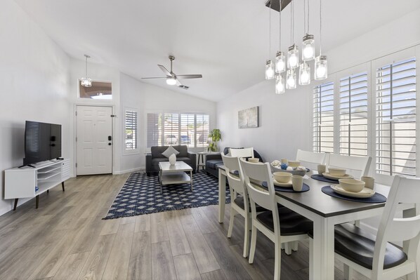 A modern living room with a dining area, white walls, and a ceiling fan. - Heated Pool Option, Close to Freeway, Hiking & Golf nearby. .Heart of Peoria! (Peoria)