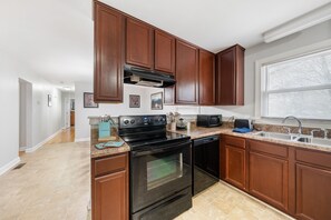 A kitchen with dark wooden cabinets, a black stove, and a dishwasher. - The Sanctuary Downtown >5mi to Downtown & Union Park (Raleigh)
