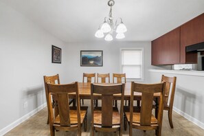 A dining area with a wooden table and chairs, a chandelier, framed pictures on the wall, and a kitchen area with wooden cabinets. - The Sanctuary Downtown >5mi to Downtown & Union Park (Raleigh)