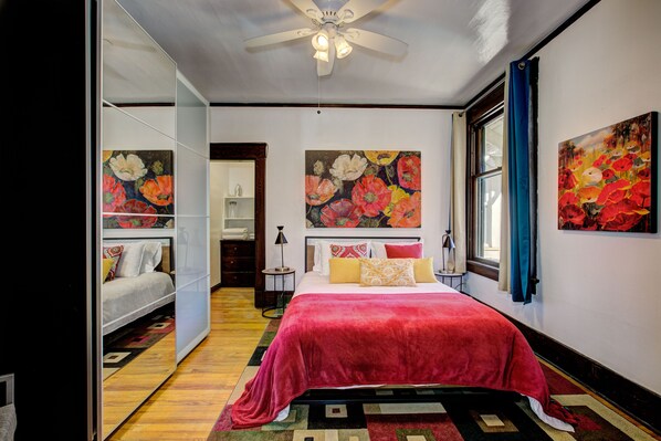 Une chambre à coucher avec un lit, un ventilateur de plafond et des œuvres d’art à motifs floraux sur les murs.