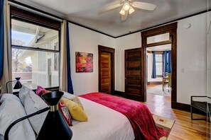 Une chambre dotée d’un grand lit, d’un ventilateur de plafond, d’une fenêtre avec des rideaux et d’une porte donnant sur un balcon.