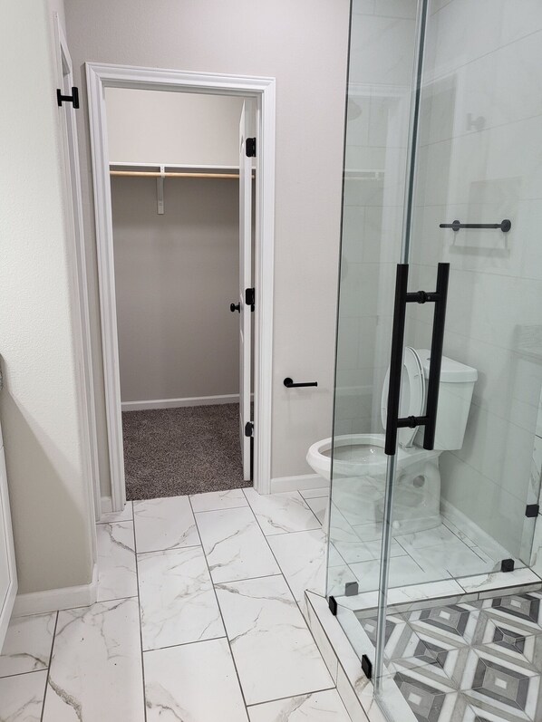 A bathroom with a glass shower enclosure, a toilet, and a white tiled floor. - 35-45 Min to Lackland AFB! Gorgeous Ranch-Style Home!  (Floresville)