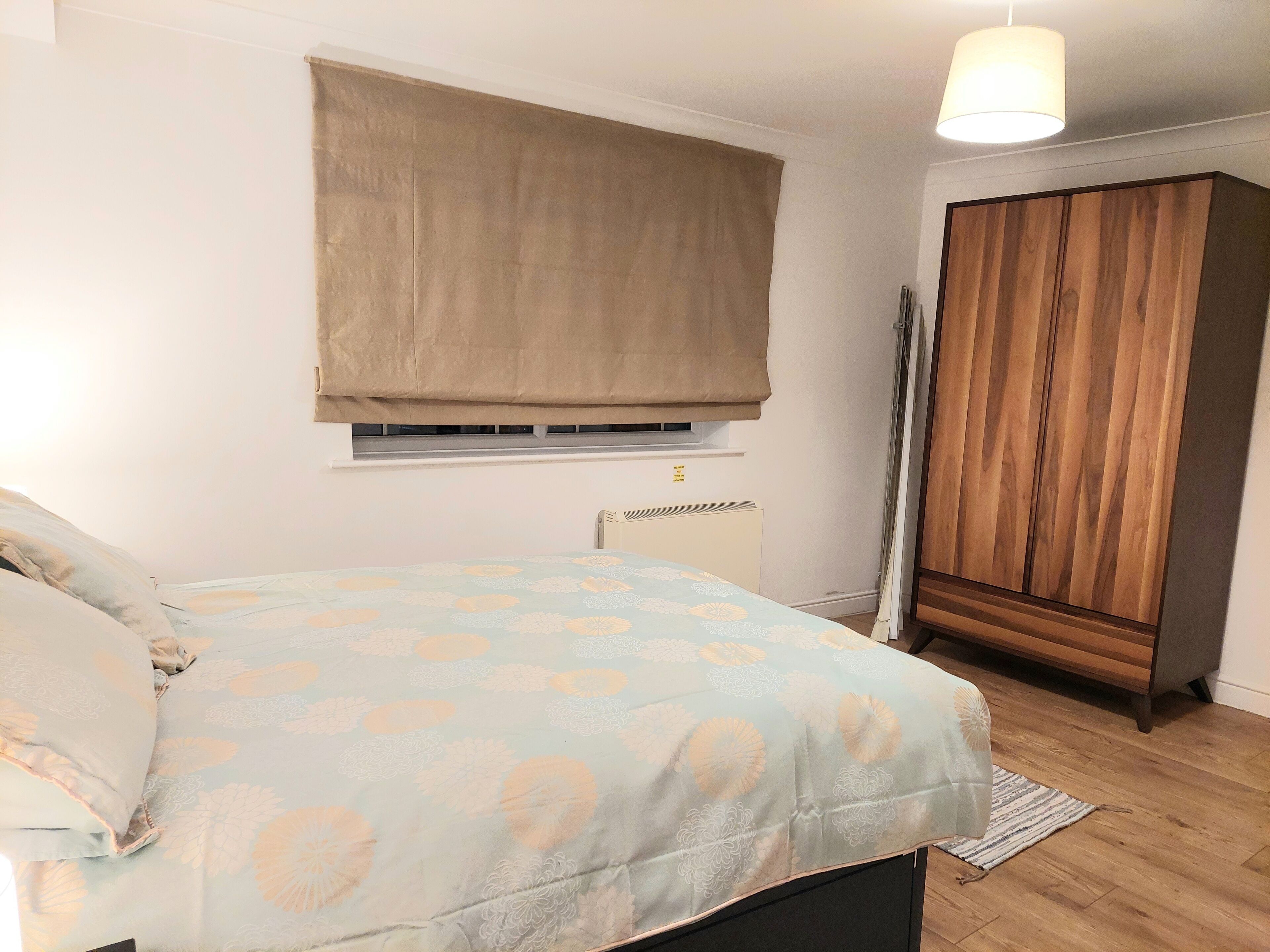 Un dormitorio con cama, ventana con persiana, radiador y armario.