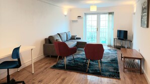 En moderne stue med en grå sofa, røde stole, et lille hvidt bord og et fjernsyn på et stativ.