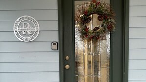 Eine dunkelgrüne Tür mit Fensterteil, Fußmatte und einem Kranz.