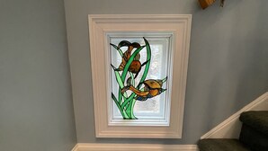 Eine Ecke mit einer grauen Wand, einem Fenster mit bleiverglasung in weißem Rahmen, das Vögel zeigt, und einer Teppich-Treppe.