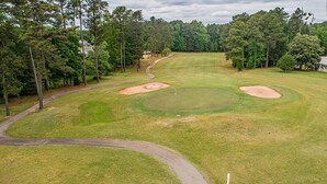 Ein Golfplatz mit Sandbunkern, einem gewundenen Weg und dichter Baumvegetation.
