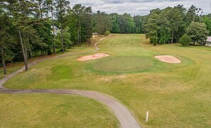 A golf course with sand bunkers, a winding path, and dense trees.
