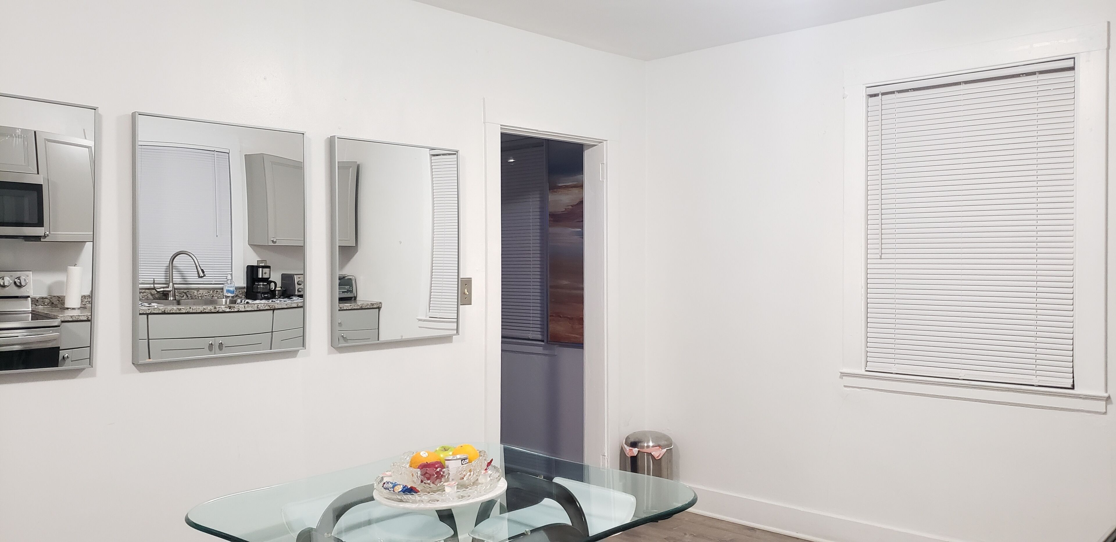 Una cocina moderna con electrodomésticos de acero inoxidable, una mesa de comedor de vidrio y un frutero, y una puerta que da a una habitación con vistas.