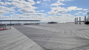 A wooden boardwalk with benches and a covered area, leading to a beach.