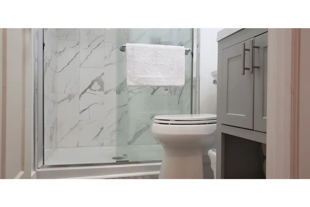 Une salle de bain avec une douche à parois de verre, des toilettes blanches et un meuble avec des poignées.
