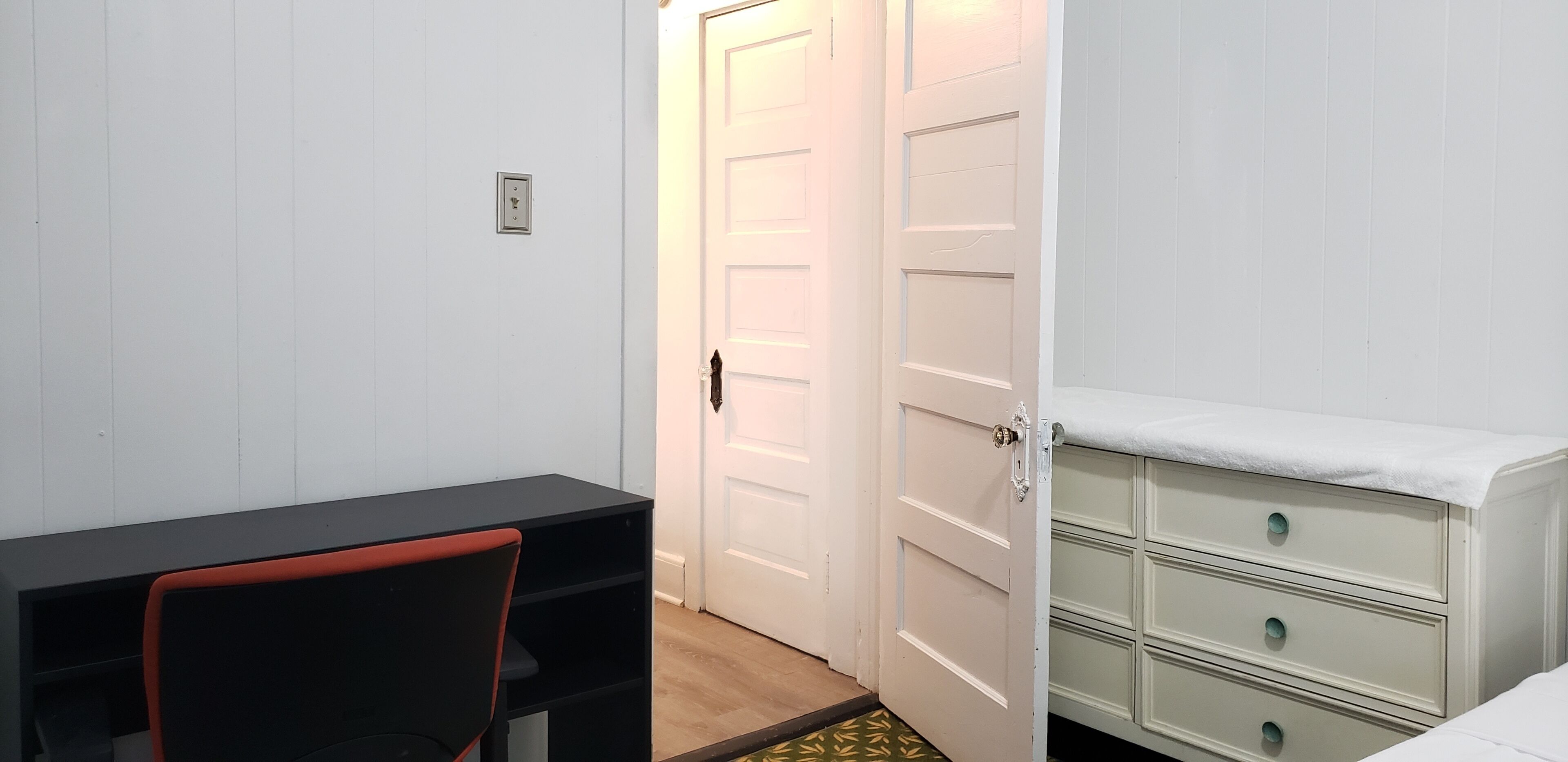 A room with a desk, chair, and a dresser with drawers.