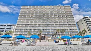 A large hotel with multiple balconies, a beach area with umbrellas, and palm trees. - Breathtaking Views Oceanfront 2 Bed 2 Bath Condo Water's Edge Resort Garden City (Murrells Inlet)