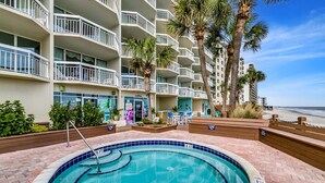 A hotel pool area with a hot tub, surrounded by a brick deck and palm trees. - Breathtaking Views Oceanfront 2 Bed 2 Bath Condo Water's Edge Resort Garden City (Murrells Inlet)