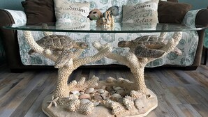 A glass coffee table with a sea turtle centerpiece, a patterned sofa, and decorative pillows. - Breathtaking Views Oceanfront 2 Bed 2 Bath Condo Water's Edge Resort Garden City (Murrells Inlet)