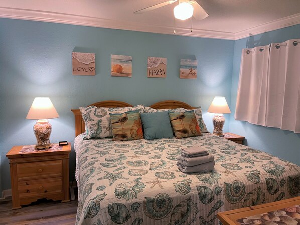 A bedroom with a bed, two nightstands, a ceiling fan, and wall art.