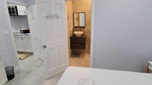 A bedroom with a bed, a bathroom with a sink and mirror, and a kitchen area with cabinets and appliances. - Yamabeach Stays (Nassau)
