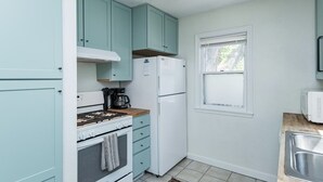 Une cuisine de taille réduite avec des meubles de couleur turquoise, un réfrigérateur blanc, une cuisinière et une fenêtre.