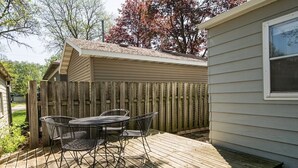 Une terrasse en bois avec une table et des chaises en métal, une clôture en bois et une maison avec une fenêtre.
