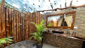 A bathroom with a bamboo wall, a stone wall, a sink, a mirror, and a potted plant. - Celeste Glamping Guatape (Guatapé)