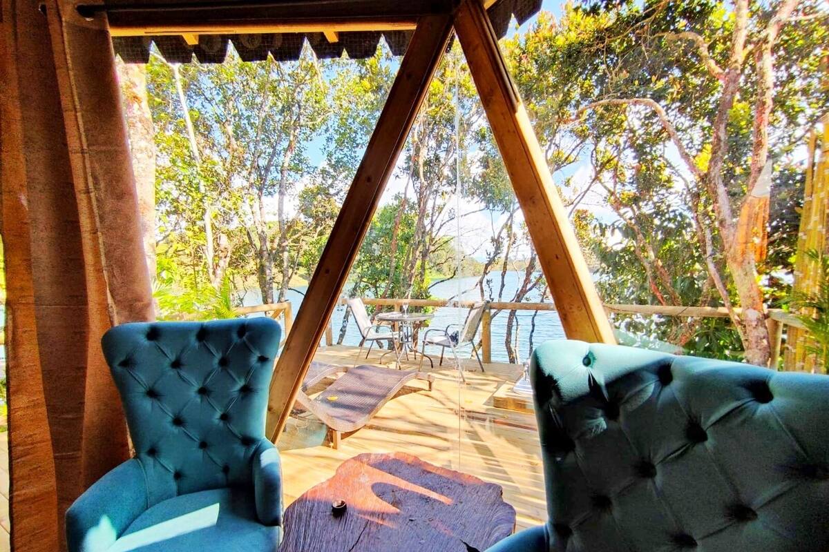 Une terrasse en bois avec deux chaises bleues rembourrées et une petite table, donnant sur une étendue d’eau et des arbres.