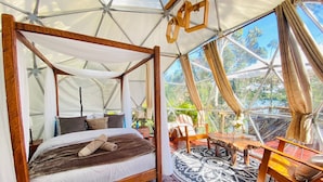 A four-poster bed with a canopy, a wooden floor, and a view of the outdoors through a glass structure. - Celeste Glamping Guatape (Guatapé)