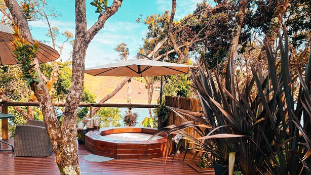 A wooden deck with a hot tub, outdoor furniture, and a large umbrella. - Celeste Glamping Guatape (Guatapé)