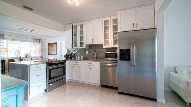 A modern kitchen with white cabinets, stainless steel appliances, and a large refrigerator.