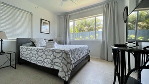 A bedroom with a bed, a desk, a ceiling fan, and a window with curtains.