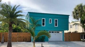 A turquoise two-story house with a white garage door, surrounded by a wooden fence and palm trees. - [escape to paradise] siesta key beach getaway (Siesta Key)