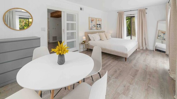A modern bedroom with a bed, a bedside table, a round dining table with chairs, and a large window with curtains. - [escape to paradise] siesta key beach getaway (Siesta Key)
