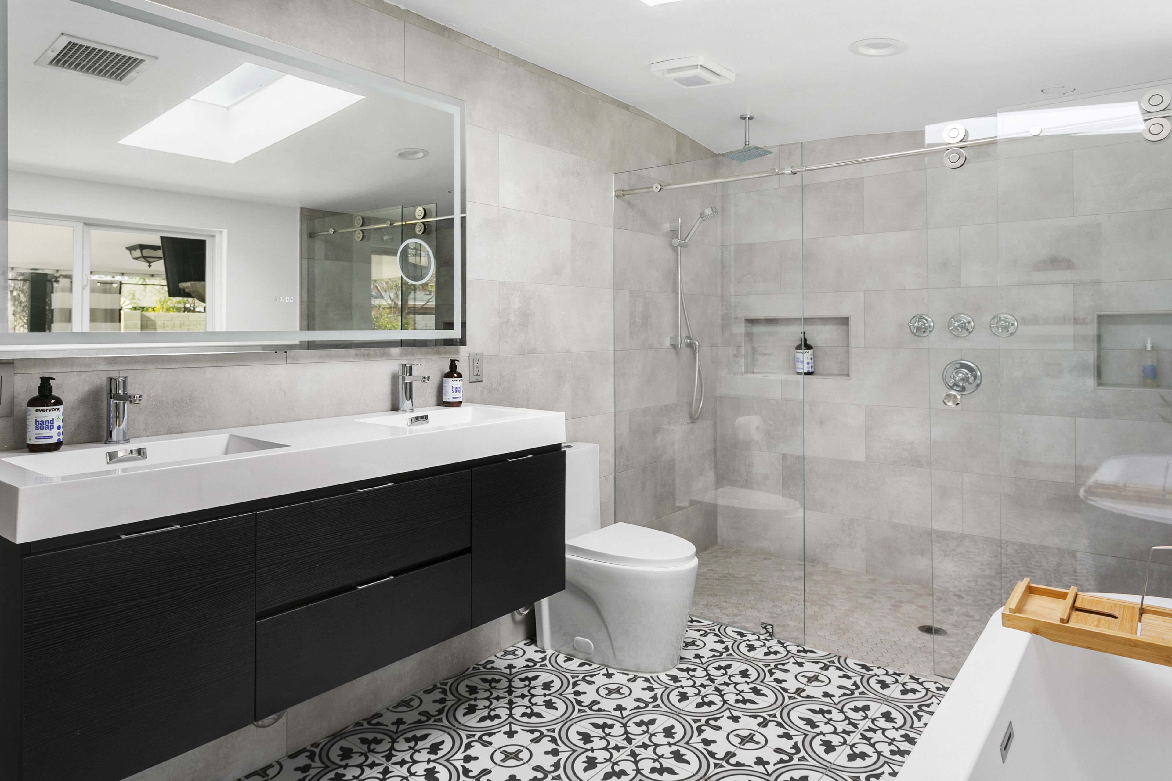 A modern bathroom with a double sink vanity, a glass shower enclosure, and patterned floor tiles.