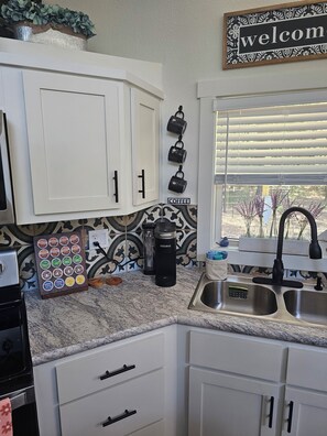 A kitchen with white cabinets, a coffee maker, and a welcome sign.