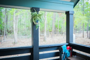 Une terrasse en bois agrémentée d’une plante suspendue, d’un banc avec une serviette bleue, et offrant une vue sur une forêt.