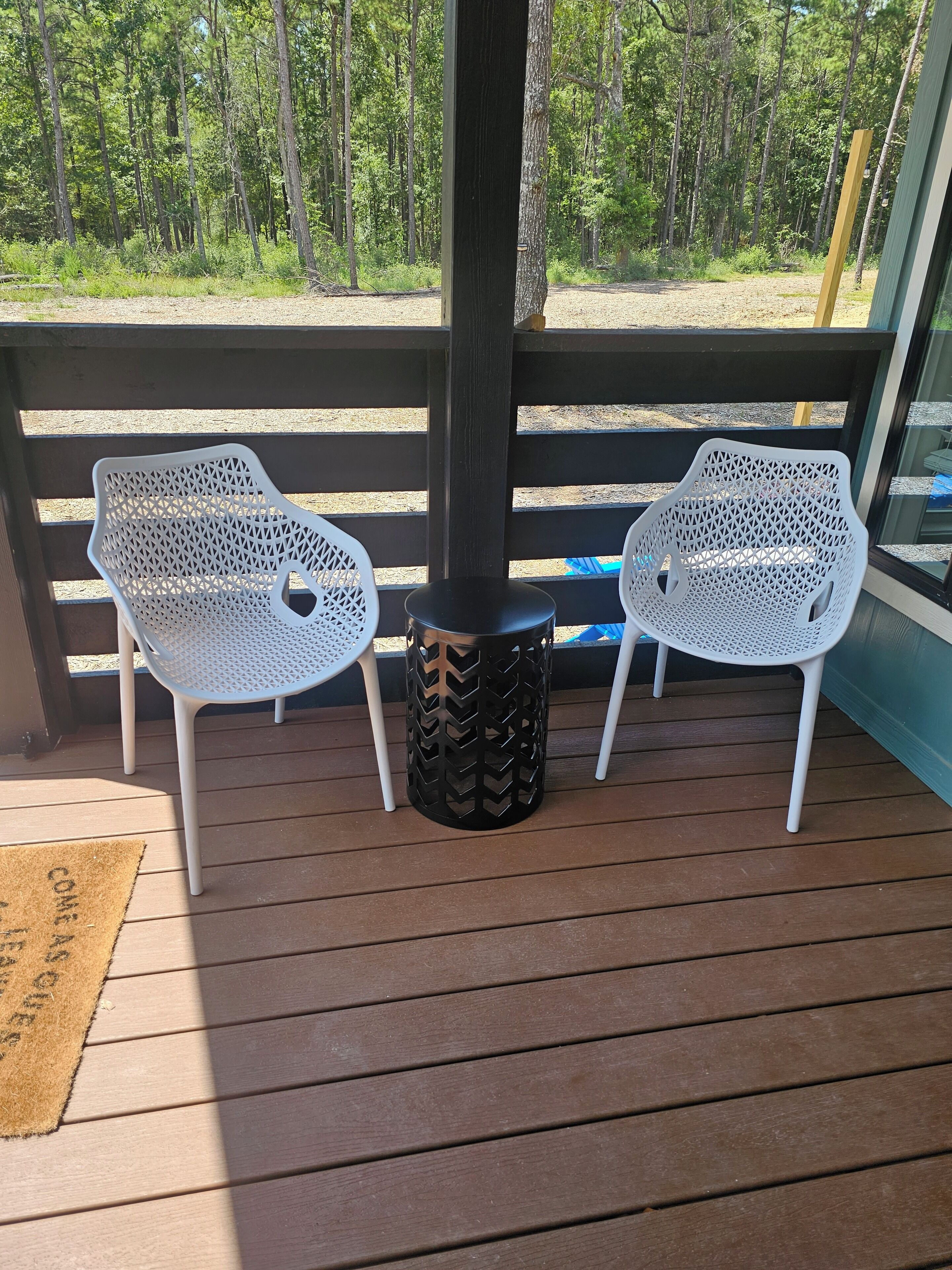 Une terrasse en bois avec deux chaises en résille blanche et une poubelle noire.